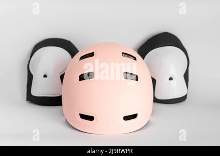Draufsicht auf Rollschuhe Schutzausrüstung Set - Helm und Kniepolster rosa Farben. Weiß-grauer Hintergrund, Seitenansicht Stockfoto