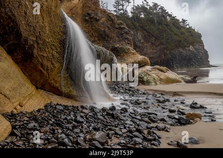 Der Wasserfall von Fall Creek fließt an stürmischen Tagen am Hug Point in der Nähe von Cannon Beach, Oregon, USA, in den Strand Stockfoto