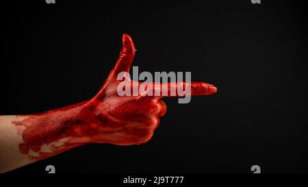 Die blutige Hand einer Frau zeigt eine Geste einer Waffe auf schwarzem Hintergrund. Stockfoto