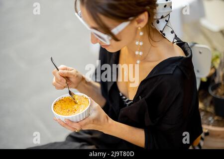 Frau, die im Restaurant im Freien Dessert mit Creme Brulee isst Stockfoto