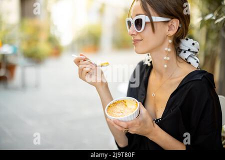 Frau, die im Restaurant im Freien Dessert mit Creme Brulee isst Stockfoto