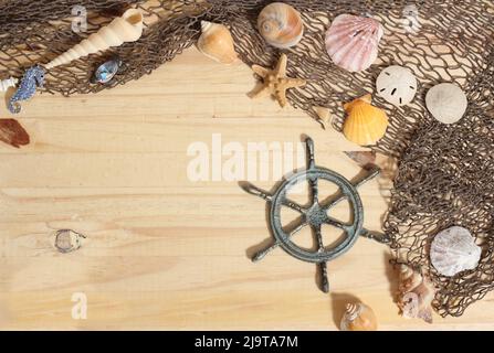 Kapitänsrad mit Fischernetz und Muscheln auf Holz Hintergrund Stockfoto