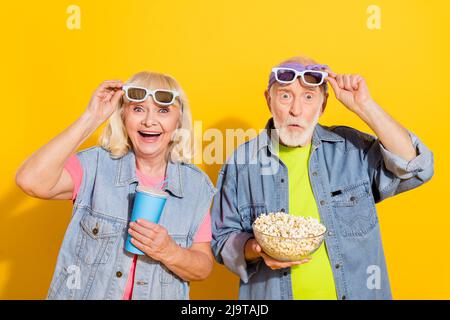 Foto von niedlichen überrascht Ehemann Frau tragen Jeans Hemden beobachten Comedy essen Popcorn isoliert gelbe Farbe Hintergrund Stockfoto