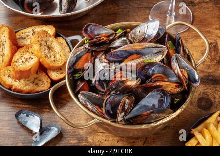 Miesmuscheln-Abendessen in einem französischen Restaurant mit Wein und geröstetem Brot auf einem rustikalen Holztisch Stockfoto