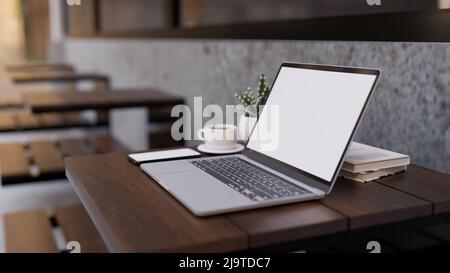 Notebook Laptop Computer White Screen Mockup, Buch, Smartphone, eine Tasse Kaffee und Dekorpflanze auf Holztisch im modernen Café. Nahaufnahme 3D Stockfoto