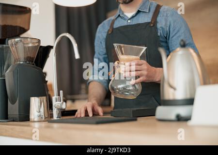 Der Barista hält in seinen Händen ein Glasgefäß für die Zubereitung von Filterkaffee Stockfoto