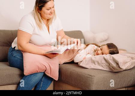 Die fürsorgliche Mutter las abends ein Buch über ihre kleine Tochter, während das Mädchen schlief und ihren Kopf auf das Kissen legte. Stockfoto