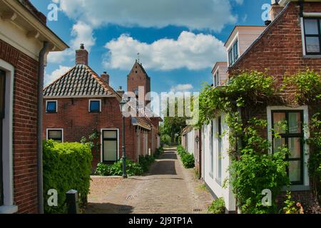 Schmale Straße mit alten Häusern und einem Kirchturm im traditionellen niederländischen Dorf Garnwerd, Provinz Groningen, Niederlande Stockfoto