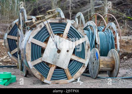 Große Holzspulen mit Gummibändern und elektrischen Kabeln auf Lager. Stockfoto