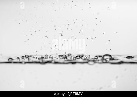 Frische und kohlensäurehaltige Wassertropfen, die auf einer transparenten Flüssigkeit mit Blasen schwimmen Stockfoto