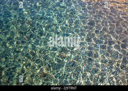 Textur aus transparentem türkisblauem plätscherndem Wasser des Meeres mit kleinen Steinen unter der Oberfläche Stockfoto