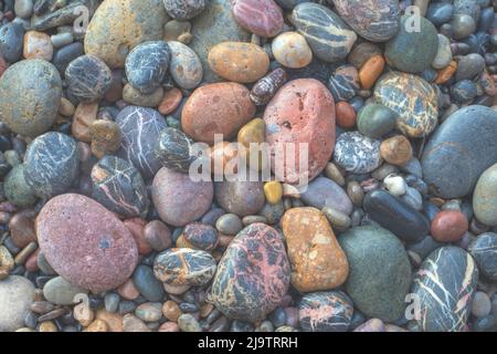 Nahaufnahme von Steinen am Ufer des Strandes in verschiedenen Größen, Farben und Texturen, die vom Wasser des Meeres nass werden Stockfoto