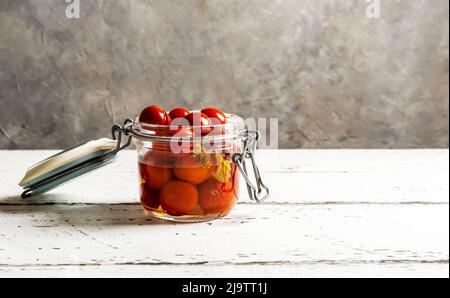 Eingelegte Tomaten in einem Glas auf weißem Holztisch mit grauem Hintergrund und Kopierraum Stockfoto