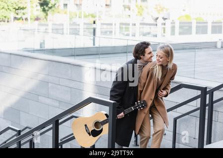 Junger Mann mit Akustikgitarre und stilvoller blonder Frau, die in der Stadt unterwegs ist Stockfoto