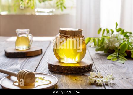 Akazienhonig im Glasgefäß mit Holzdipper und Blumen auf Holzhintergrund zur Seite Stockfoto