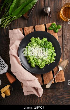 Italienisches Risotto. Köstliches Risotto mit Pesto-Sauce oder Bärlauch-Pesto, Basilikum, Parmesankäse und einem Glas Weißwein auf altem Holztisch Stockfoto