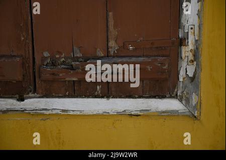 Altes traditionelles Landhaus antike hölzerne Fensterläden mit einer weißen Verkleidung, abgebrochener Farbe und rostigen Scharnieren gegen eine ockerfarbene Stuckwand. Stockfoto