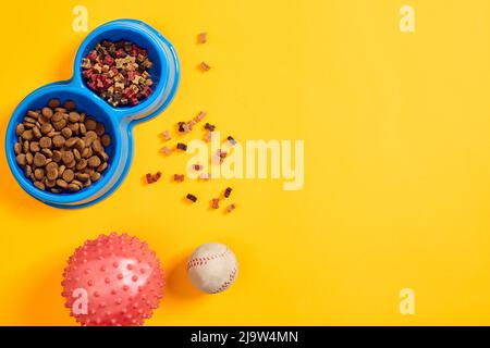 Trockenes Tierfutter in Schüssel mit einem Ball auf gelbem Hintergrund Draufsicht Stockfoto