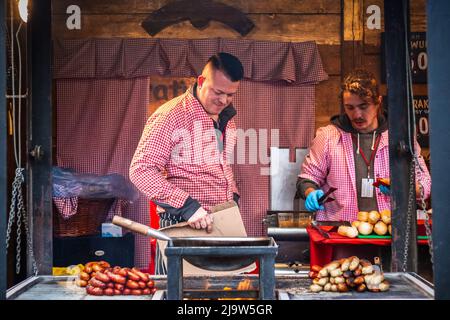 London, Großbritannien - 2. Dezember 2021 - zwei männliche Mitarbeiter verkaufen Hot Dogs auf dem Weihnachtsmarkt Hyde Park Winter Wonderland Stockfoto