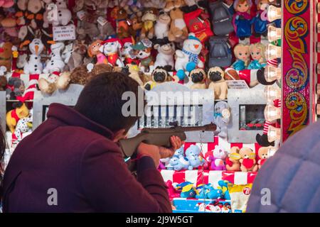 London, Großbritannien - 2. Dezember 2021 - Touristen spielen ein Schießspiel, um auf dem Weihnachtsmarkt Hyde Park Winter Wonderland Stofftiere an der Wand zu gewinnen Stockfoto