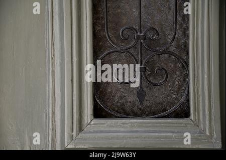 Altes neoklassizistisches Haus, Eingangstür aus olivgrünem Holz mit handgefertigten schmiedeeisernen Gittern auf einem strukturierten Glas. Stockfoto