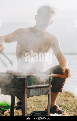 Porträt eines lächelnden Mannes, der Fleisch auf dem Grill würzt. Hübscher Mann, der Grill zubereitet und Rindfleisch auf der Grillparty im Freien für einen Freund zubereitet. Nahaufnahme Hand gri Stockfoto