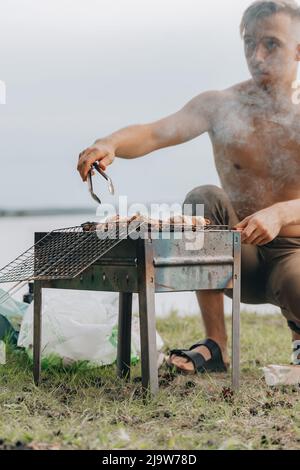 Porträt eines lächelnden Mannes, der Fleisch auf dem Grill würzt. Hübscher Mann, der Grill zubereitet und Rindfleisch auf der Grillparty im Freien für einen Freund zubereitet. Nahaufnahme Hand gri Stockfoto