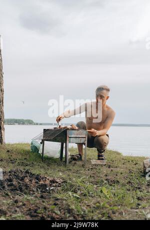 Porträt eines lächelnden Mannes, der Fleisch auf dem Grill würzt. Hübscher Mann, der Grill zubereitet und Rindfleisch auf der Grillparty im Freien für einen Freund zubereitet. Nahaufnahme Hand gri Stockfoto