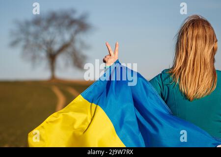 Frau mit ukrainischer Flagge ist eine Hand, die Frieden oder Sieg symbolisiert. Stockfoto