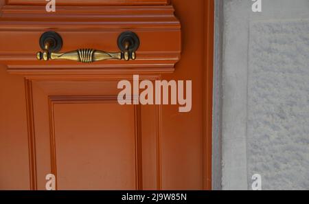 Alte neoklassische Haus tangerine orange hölzerne Eingangstür mit einem antiken Messinggriff an einer Steinwand. Stockfoto