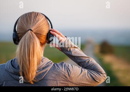 Frau mit Kopfhörern, die sich zum Laufen auf der Straße bereit gemacht hat. Joggen und Fitnessaktivitäten im Freien Stockfoto