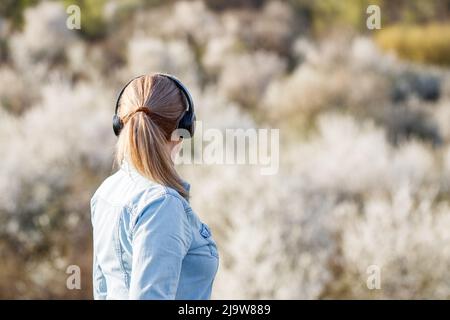 Frau mit Kopfhörern hört Musik im Freien. Weibliche Person entspannend und genießen Frühling Natur Stockfoto