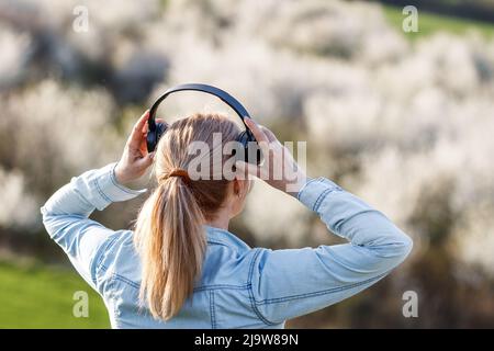 Frau mit Kopfhörern hört Musik im Freien. Weibliche Person entspannend und genießen Frühling Natur Stockfoto