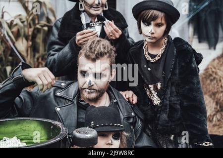 Beängstigende Familie, Mutter, Vater, Töchter, die Halloween feiern. Kessel des Trank. Erschreckende schwarze Schädel Halbgesicht Make-up, Hexe Kostüme, stilvolle Bild Stockfoto