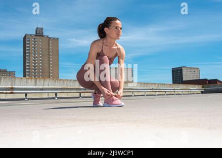 Sportliche Frau, die ihre Laufschuhe vor dem Training bindet, urbane Umgebung. Stockfoto