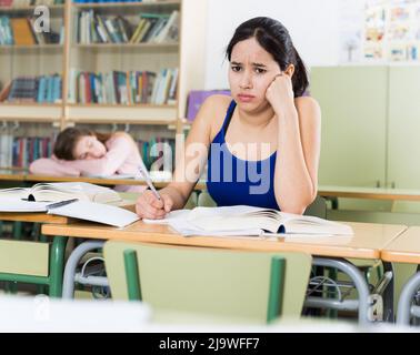 Das junge Mädchen denkt über schwierige Aufgaben am Schreibtisch nach Stockfoto