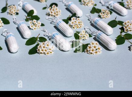 Medizinisches weibliches Tampon und weiße Blüten auf blauem Hintergrund. Hygienischer weißer Tampon für Frauen. Wattestäbchen. Menstruation, Heilmittel. Patern. Stockfoto