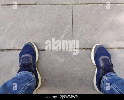 Männerbeine in Jeans und zerrissene blaue Sneaker auf Betonboden Stockfoto