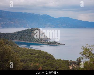 Reise zur Lagune in Oludeniz, Fethiye, Türkei. Strand in der Nähe von Darbogaz. Mit Blick auf den Berg Babadag, Winterlandschaft mit Bergen, grünem Wald, azurblauem Wasser, Strand und bewölktem Himmel Stockfoto