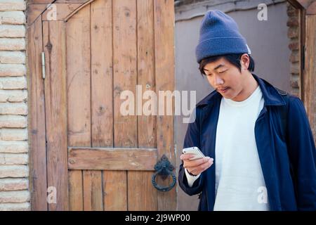 Netter Tourist aus Korea mit einem Rucksack, der in das Telefon schaut Stockfoto