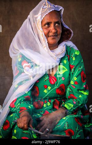 Alte Frau in weißem Schal und leuchtend grünem Kleid in Asmara Stockfoto