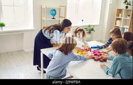 Schüler und Lehrer stehen um den Tisch und verbinden Puzzleteile Stockfoto