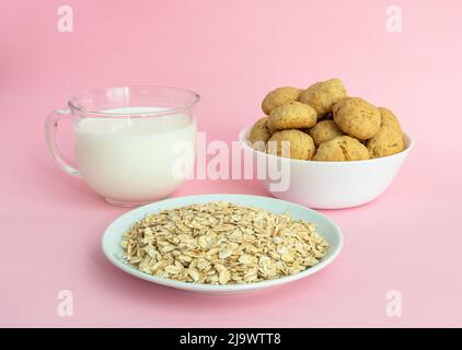 Haferflocken, Haferflocken-Kekse auf einem weißen Teller, Milch in transparentem Glas auf einem rosa Hintergrund, Seitenansicht, das Konzept der gesunden Ernährung und Herstellung von Müsli oder Keksen. Hochwertige Fotos Stockfoto