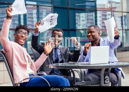 Eine Gruppe ihrer drei erfolgreichen afroamerikanischen Geschäftsleute in einem stilvollen Anzug sitzt am Tisch und arbeitet mit einem Laptop Online-Konferenz und werfen Stockfoto