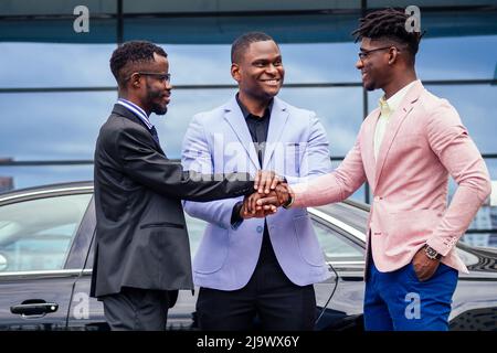 Eine Gruppe von drei stilvollen afroamerikanischen Geschäftsmann Freunde Unternehmer Mode-Business-Anzüge Treffen Handshake in einem Sommer im Freien. Konzept Stockfoto