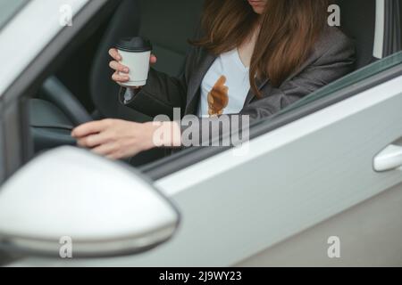 Eine Geschäftsfrau verschüttete Kaffee auf dem Hemd hinter dem Steuer eines Autos. Konzept der Reinigung Flecken auf Kleidung Stockfoto