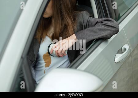Frau verschüttete Kaffee auf dem Hemd hinter dem Steuer eines Autos. Konzept der Reinigung Flecken auf Kleidung Stockfoto