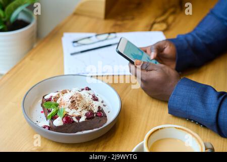 Nahaufnahme von Waffeln mit Eis und Kaffee auf dem Tisch mit einem Mann, der im Café an seinem Mobiltelefon arbeitet Stockfoto