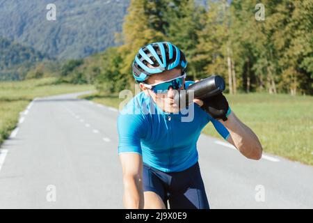 Männlicher Radfahrer, der Wasser aus der Flasche während des hochintensiven Pedalierens trinkt, Schuss verfolgt. Stockfoto