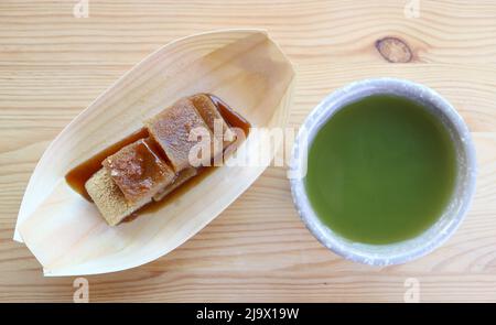 Köstliche japanische traditionelle Süßigkeit namens Warabimochi in Kuromitsu Sirup mit einer Tasse heißen Matcha Grüner Tee Stockfoto